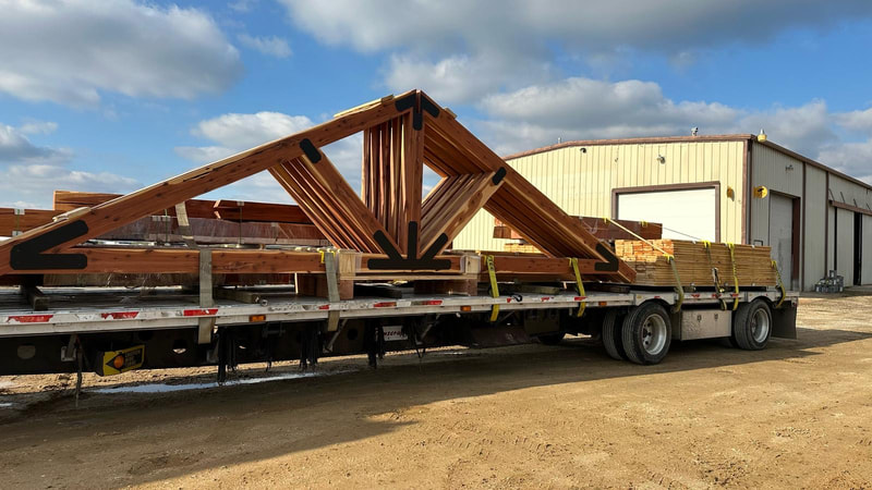 Heavy timber trusses with blackened steel plates loaded on a flatbed trailer outside our shop